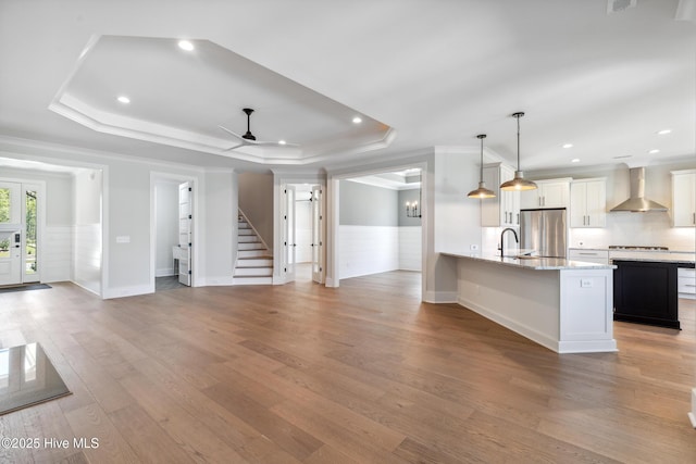 5037 Saltgrass Cv, Leland, NC 28451 - kitchen featuring wall chimney range hood, freestanding refrigerator, ornamental molding, wainscoting, and a tray ceiling