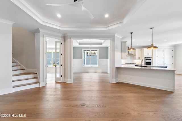 5037 Saltgrass Cv, Leland, NC 28451 - kitchen with a raised ceiling, ornamental molding, a ceiling fan, wall chimney range hood, and wood finished floors