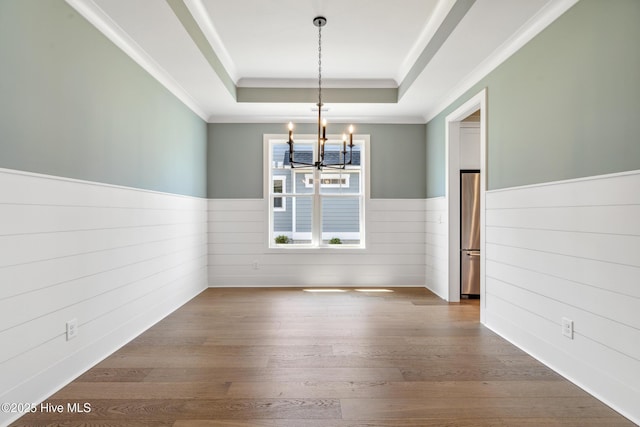 5037 Saltgrass Cv, Leland, NC 28451 - unfurnished dining area with a raised ceiling, a chandelier, a wainscoted wall, hardwood / wood-style floors, and crown molding