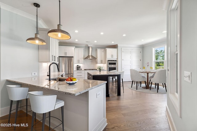 5037 Saltgrass Cv, Leland, NC 28451 - kitchen featuring wall chimney exhaust hood, a sink, appliances with stainless steel finishes, decorative backsplash, and a kitchen bar