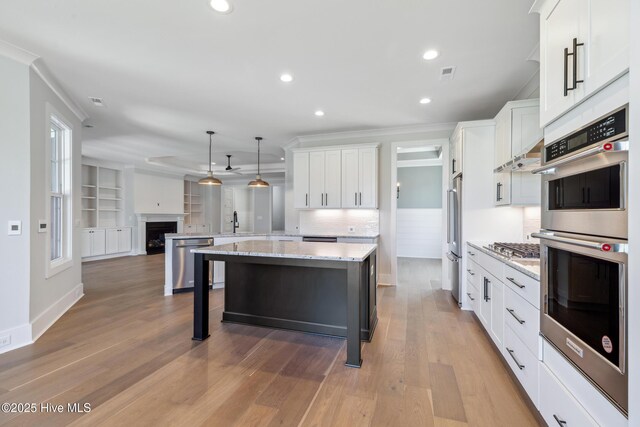 5037 Saltgrass Cv, Leland, NC 28451 - kitchen with stainless steel appliances, white cabinetry, ornamental molding, light wood-style floors, and a breakfast bar