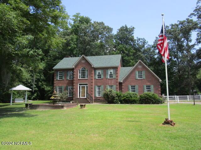 colonial inspired home featuring fence, a front lawn, and brick siding