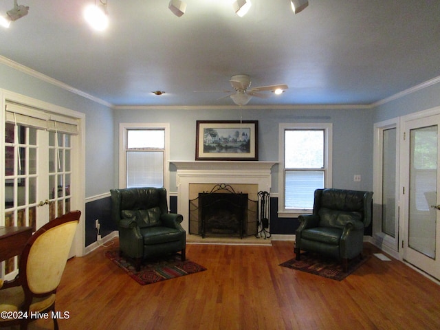 living room with a fireplace with raised hearth, ornamental molding, plenty of natural light, and wood finished floors