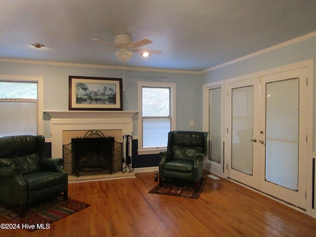 living area with a fireplace with raised hearth, french doors, wood finished floors, and crown molding