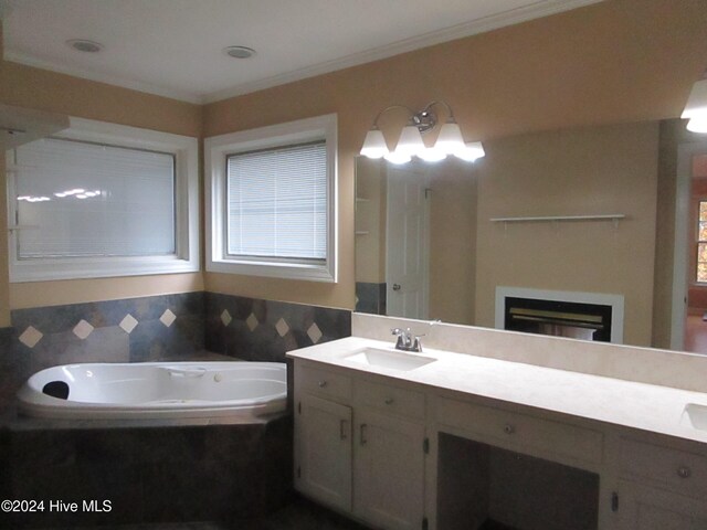 bathroom with double vanity, a glass covered fireplace, ornamental molding, a sink, and a bath