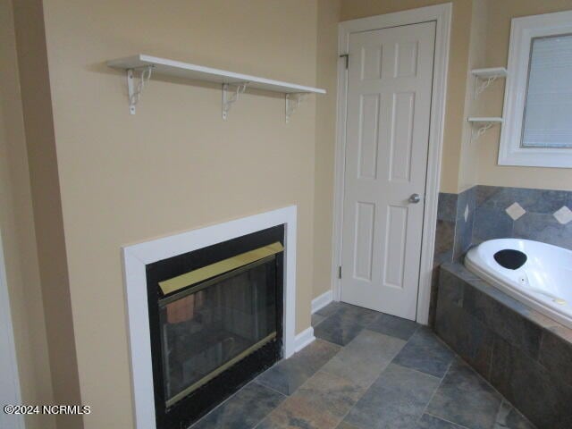 bathroom featuring a closet, a glass covered fireplace, a bath, and baseboards