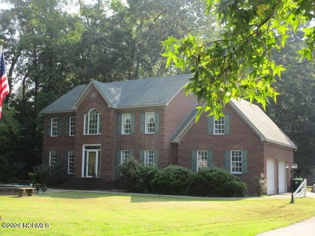 colonial-style house featuring brick siding, an attached garage, and a front lawn