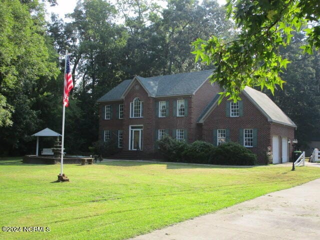 colonial home with an attached garage, driveway, brick siding, and a front yard