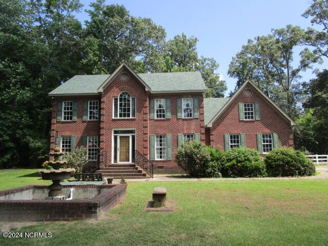 colonial inspired home featuring a shingled roof, a front yard, crawl space, and brick siding