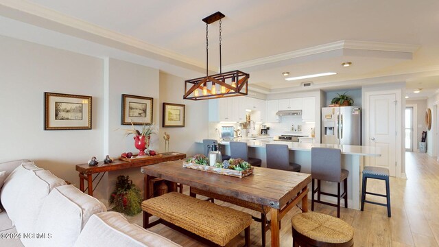 dining space featuring crown molding, light hardwood / wood-style floors, and a tray ceiling