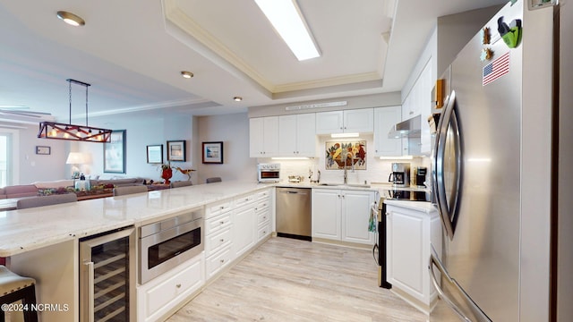 kitchen featuring light wood-type flooring, appliances with stainless steel finishes, a raised ceiling, beverage cooler, and kitchen peninsula