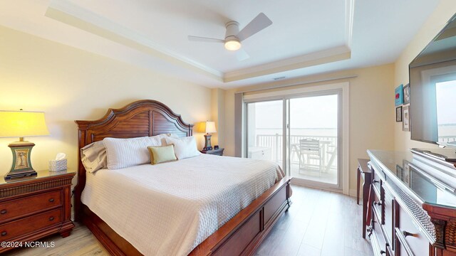 bedroom featuring a tray ceiling, light hardwood / wood-style flooring, ceiling fan, and access to exterior