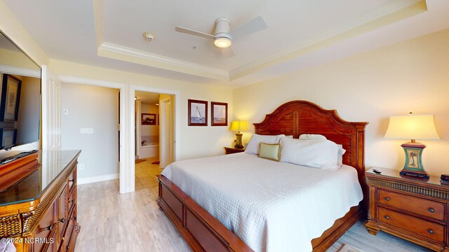 bedroom with ceiling fan, a raised ceiling, light hardwood / wood-style flooring, and connected bathroom