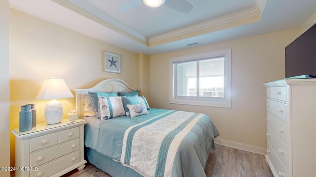 bedroom with ceiling fan, crown molding, a tray ceiling, and hardwood / wood-style floors