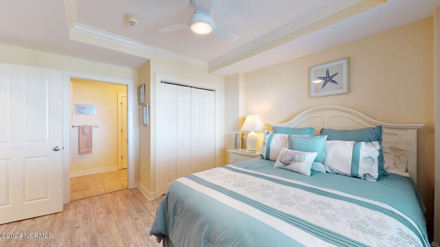 bedroom with light wood-type flooring, a closet, a tray ceiling, ceiling fan, and crown molding