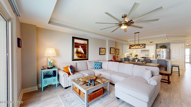 living room with a tray ceiling, ceiling fan, light hardwood / wood-style floors, and plenty of natural light