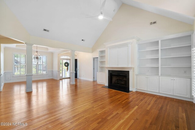 unfurnished living room with visible vents, light wood-style flooring, a fireplace with flush hearth, wainscoting, and ornate columns