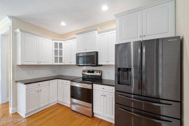 kitchen featuring stainless steel appliances, dark countertops, white cabinets, and glass insert cabinets