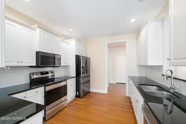 kitchen with stainless steel appliances, a sink, white cabinetry, light wood finished floors, and dark stone countertops