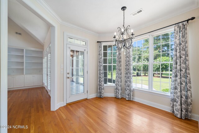 unfurnished dining area featuring baseboards, visible vents, wood finished floors, crown molding, and a chandelier