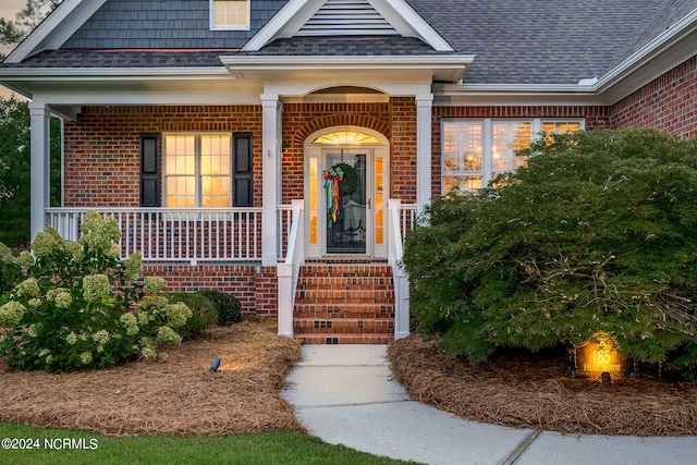 entrance to property featuring roof with shingles and brick siding