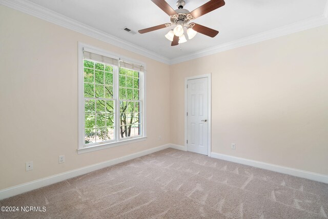 empty room with carpet floors, crown molding, visible vents, a ceiling fan, and baseboards