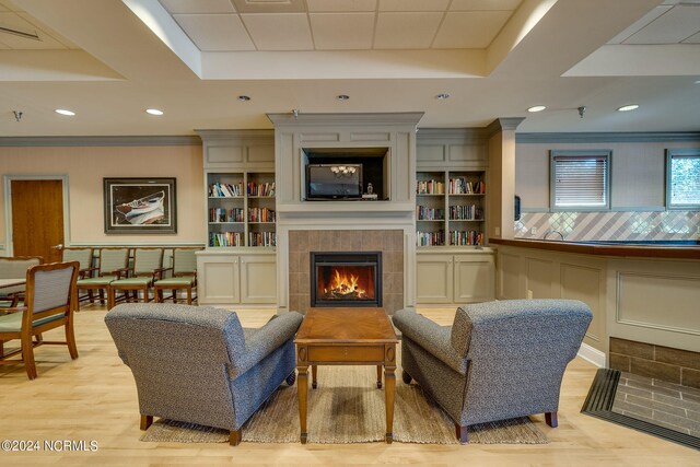 living area featuring light wood-style floors, a tray ceiling, a tiled fireplace, and ornamental molding