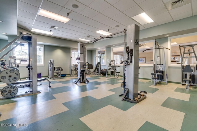 gym with a paneled ceiling, light floors, baseboards, and visible vents