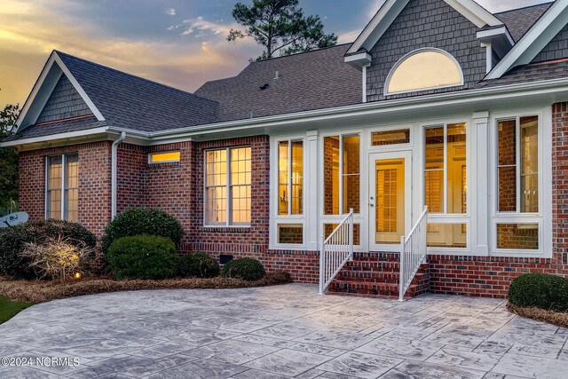 view of exterior entry with brick siding and roof with shingles