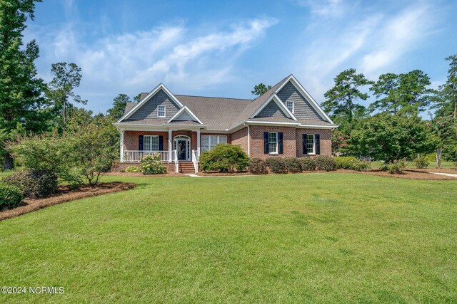 craftsman-style house with a porch, a front yard, and brick siding