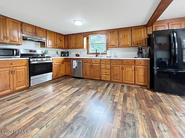 kitchen with extractor fan, appliances with stainless steel finishes, sink, and dark hardwood / wood-style floors