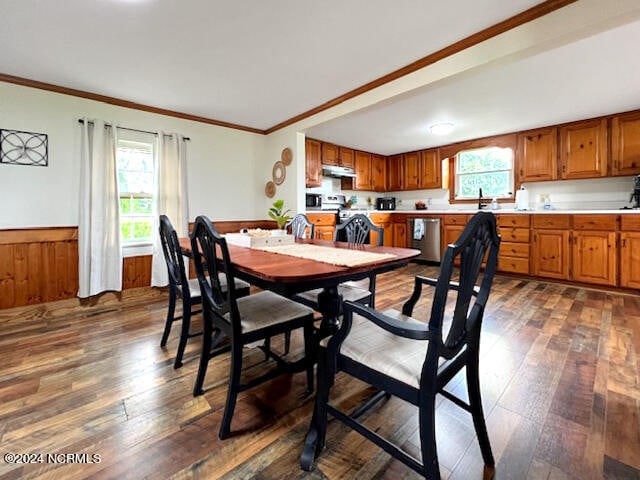 dining room featuring ornamental molding, dark wood-type flooring, a healthy amount of sunlight, and wood walls