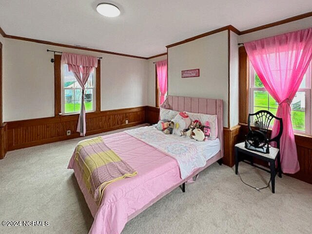 bedroom with multiple windows, wooden walls, carpet, and crown molding