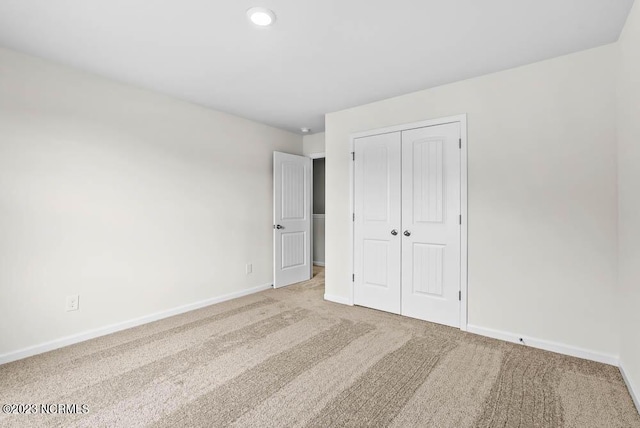 unfurnished bedroom featuring light carpet, baseboards, and a closet