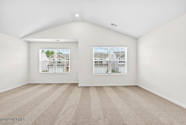 carpeted spare room featuring lofted ceiling, baseboards, and visible vents