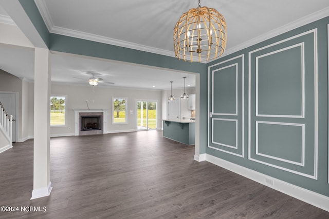 unfurnished living room with ornamental molding, ceiling fan with notable chandelier, a high end fireplace, and dark wood-type flooring