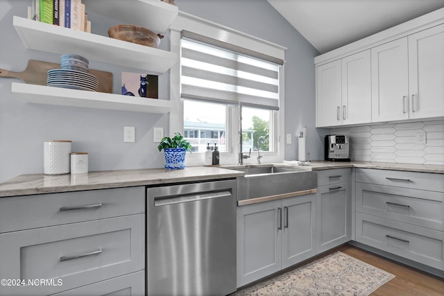 kitchen with vaulted ceiling, gray cabinets, stainless steel dishwasher, open shelves, and a sink