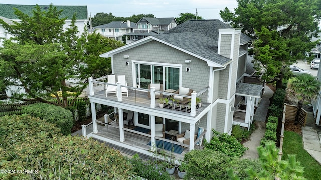 back of property with a shingled roof, an outdoor living space, a residential view, and a balcony