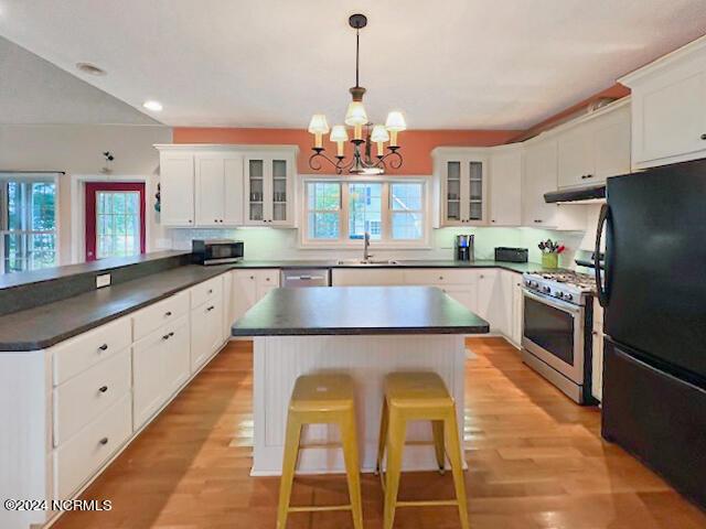 kitchen featuring stainless steel appliances, dark countertops, white cabinetry, a peninsula, and under cabinet range hood