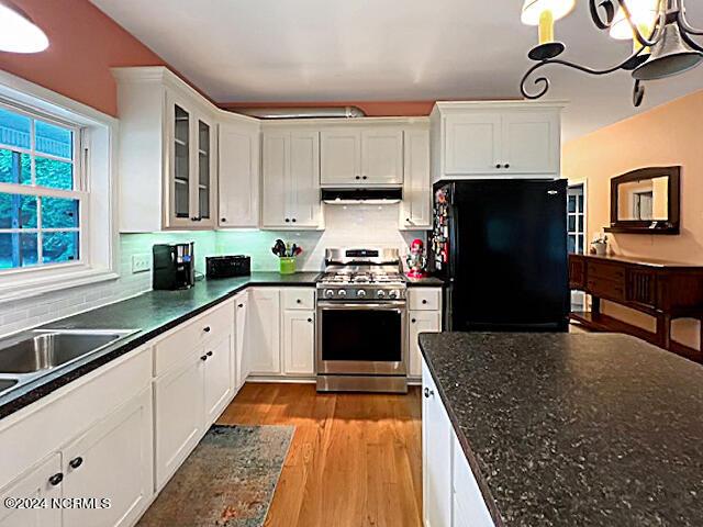 kitchen with under cabinet range hood, light wood-style floors, white cabinets, freestanding refrigerator, and stainless steel gas stove