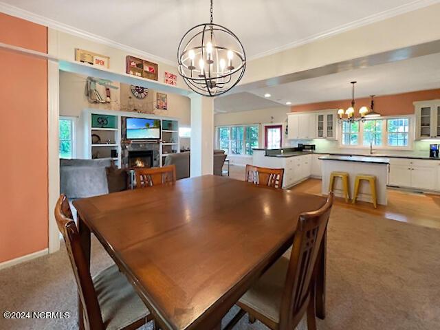 dining area featuring a chandelier, a warm lit fireplace, a wealth of natural light, and crown molding