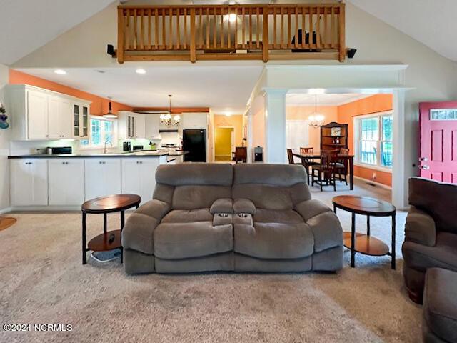 living area with light carpet, high vaulted ceiling, a chandelier, and decorative columns