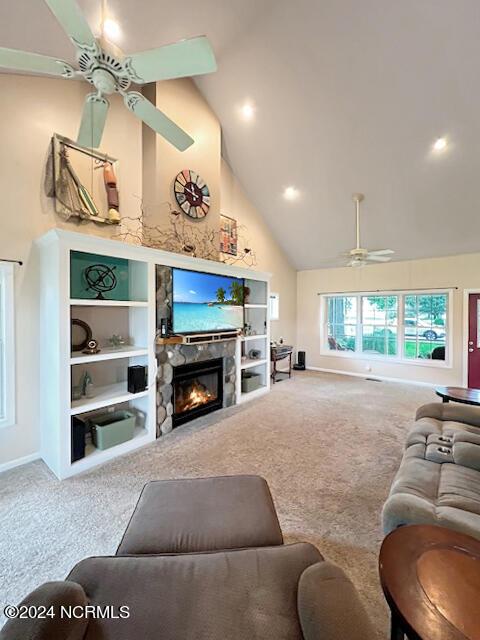 carpeted living area featuring built in features, baseboards, a ceiling fan, a stone fireplace, and high vaulted ceiling