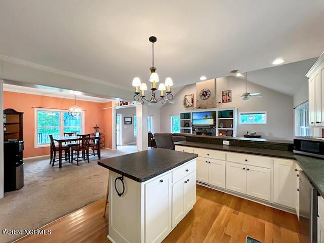 kitchen with dark countertops, stainless steel microwave, open floor plan, white cabinetry, and a peninsula