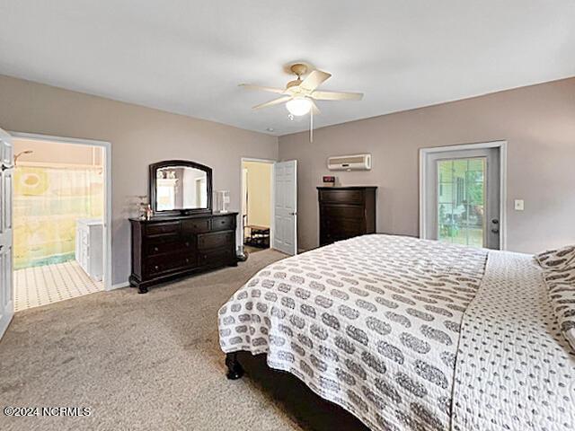 bedroom featuring carpet floors, a wall unit AC, ensuite bath, and a ceiling fan