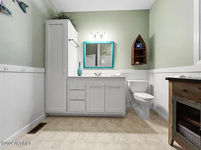 full bathroom with visible vents, wainscoting, toilet, vanity, and a fireplace