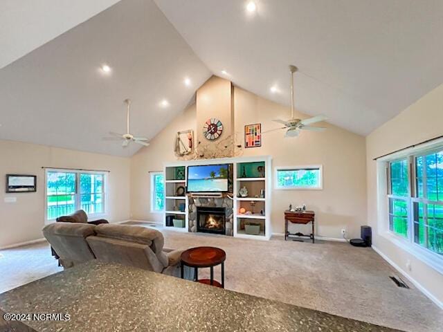 carpeted living area with visible vents, a glass covered fireplace, ceiling fan, high vaulted ceiling, and baseboards