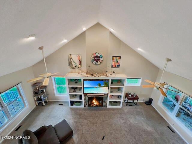 unfurnished living room with ceiling fan, a lit fireplace, carpet, and lofted ceiling