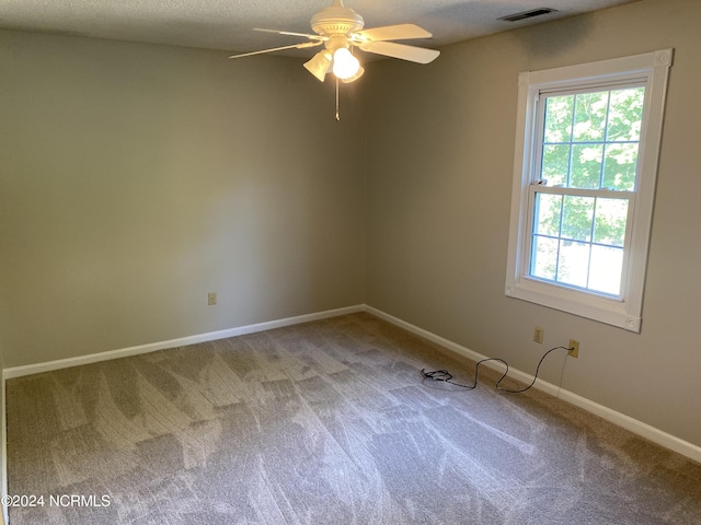 empty room with a textured ceiling, carpet flooring, a ceiling fan, visible vents, and baseboards