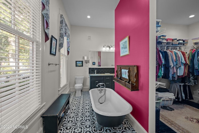 bathroom with toilet, a freestanding tub, a healthy amount of sunlight, and tile patterned floors